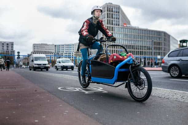 A single mother riding a cargo bike on a cycle path, carrying her child in the front.