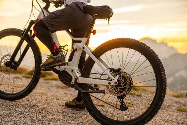 Close-up woman with sports clothing and shorts taking a break from her biking trip,standing with her bike next to the road during sunrise, side view