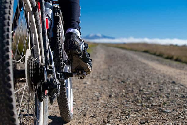 Mountain Biker On Gravel Road With Snow-peaks Ahead, Otago, New Zealand