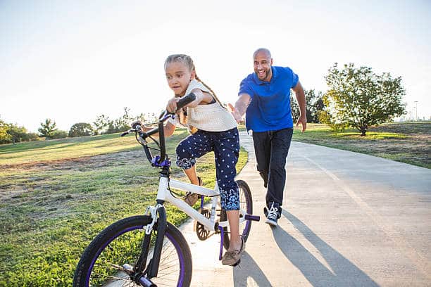 father helping his kid ride a bike
